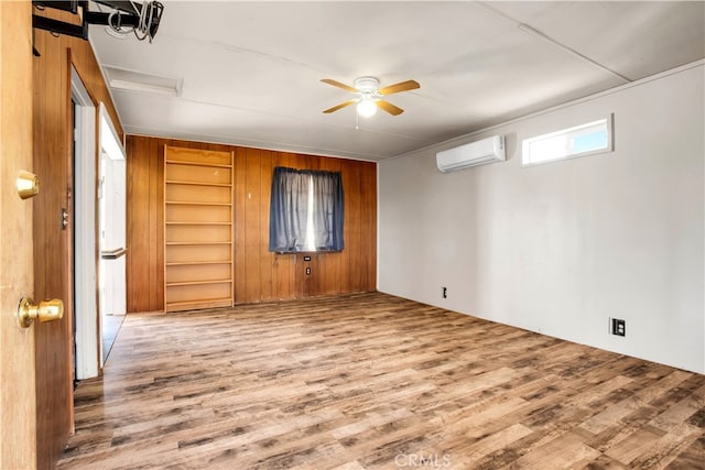 empty room featuring ceiling fan, wood-type flooring, an AC wall unit, built in features, and wooden walls