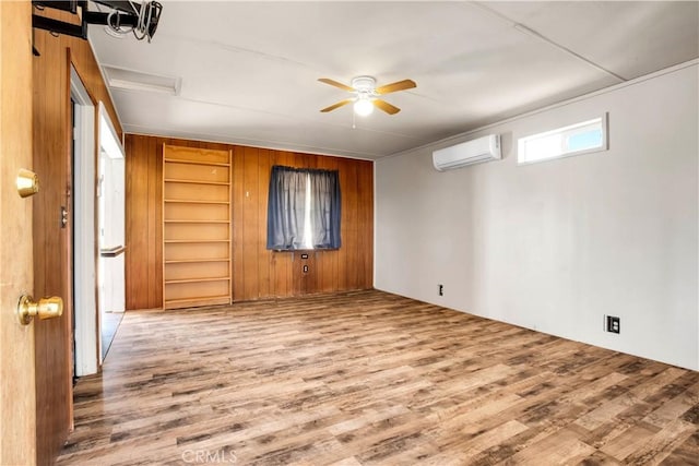 spare room featuring wood walls, attic access, a ceiling fan, wood finished floors, and a wall mounted AC