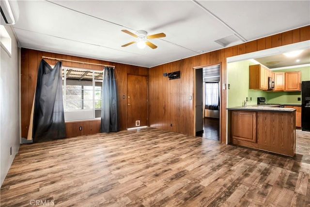 kitchen with stove, hardwood / wood-style floors, wood walls, black refrigerator, and ceiling fan