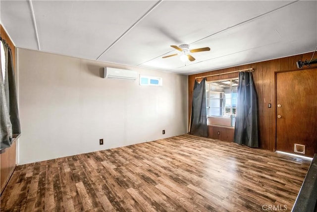 empty room featuring an AC wall unit, ceiling fan, wood finished floors, and wooden walls