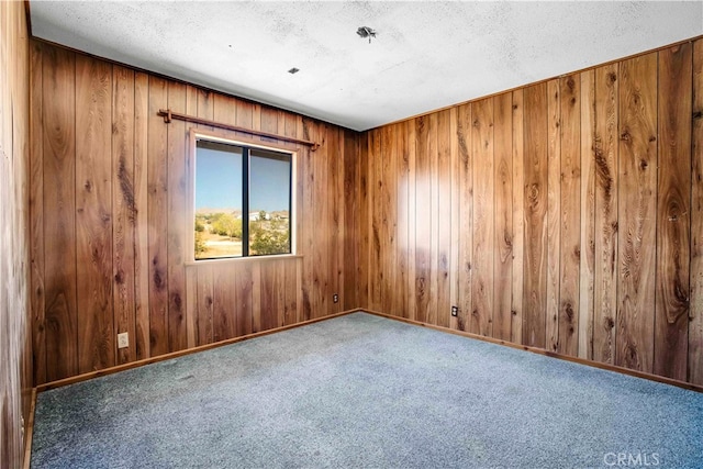 carpeted empty room featuring a textured ceiling and wood walls