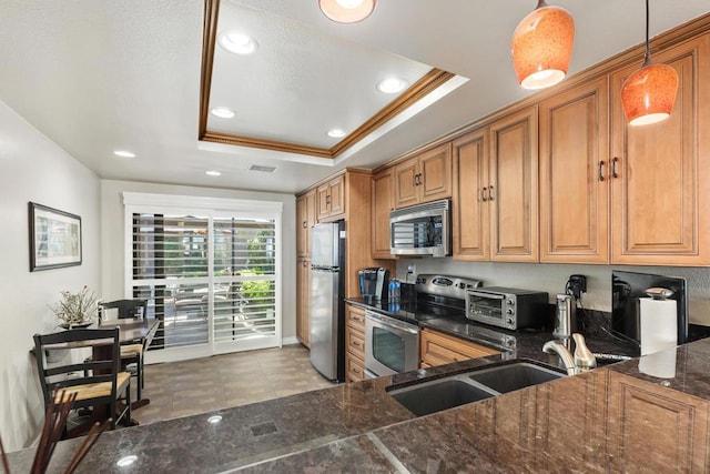 kitchen with sink, a raised ceiling, pendant lighting, appliances with stainless steel finishes, and ornamental molding