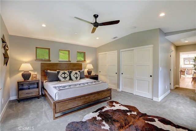 bedroom featuring ceiling fan, vaulted ceiling, light carpet, and two closets