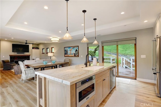 kitchen featuring stainless steel appliances, a raised ceiling, light wood-type flooring, ceiling fan, and a center island with sink