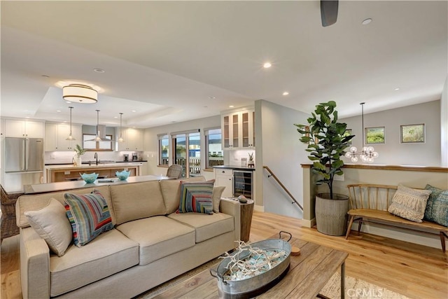 living room with wine cooler, sink, a raised ceiling, and light hardwood / wood-style floors