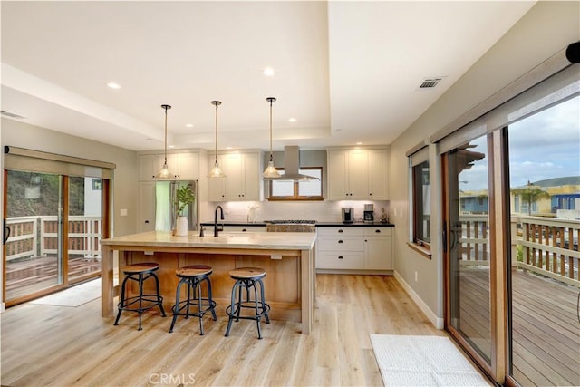 kitchen with exhaust hood, decorative light fixtures, a kitchen island with sink, light wood-type flooring, and a breakfast bar