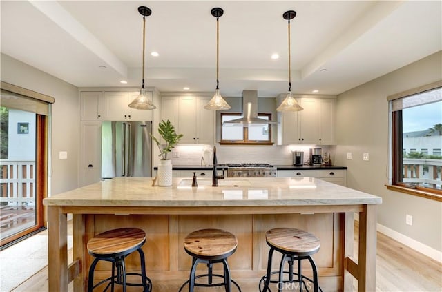 kitchen with white cabinetry, light stone countertops, high quality fridge, and wall chimney range hood