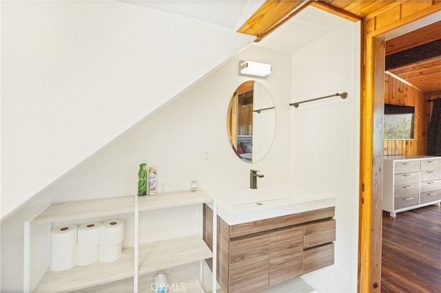 bathroom featuring wood walls, hardwood / wood-style floors, vanity, and vaulted ceiling