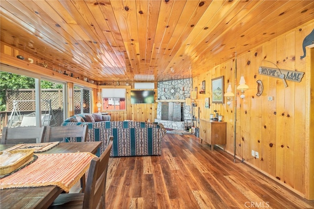 dining room with wood walls, a stone fireplace, wood ceiling, and dark wood-type flooring