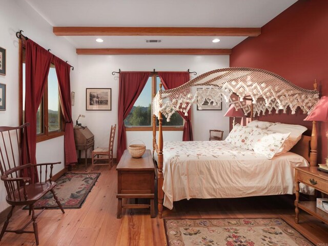 bedroom featuring beamed ceiling, hardwood / wood-style flooring, and multiple windows