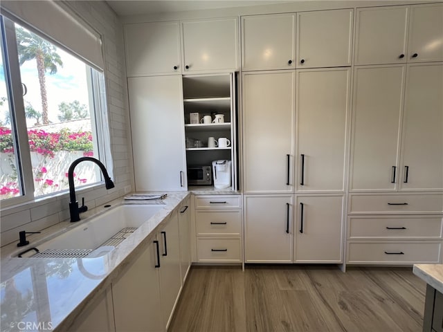 kitchen with white cabinets, decorative backsplash, sink, light hardwood / wood-style floors, and light stone counters