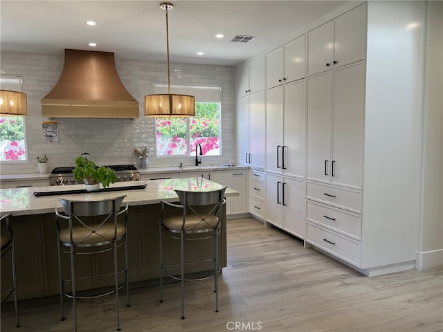 kitchen with pendant lighting, white cabinets, wall chimney range hood, decorative backsplash, and a breakfast bar