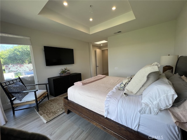 bedroom with light hardwood / wood-style floors and a tray ceiling