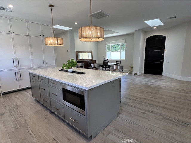 kitchen featuring pendant lighting, a center island, gray cabinetry, stainless steel microwave, and light hardwood / wood-style flooring