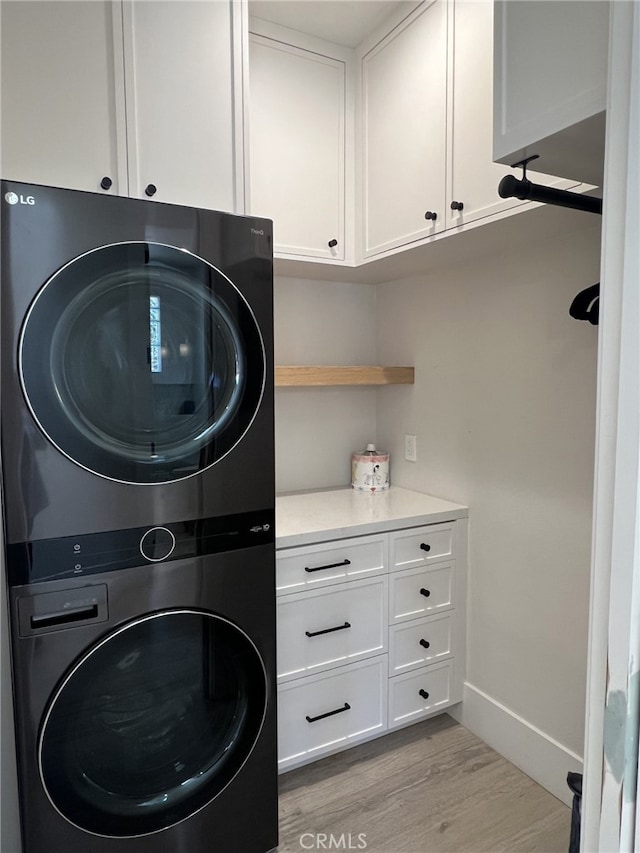 clothes washing area featuring light hardwood / wood-style floors, cabinets, and stacked washer / drying machine