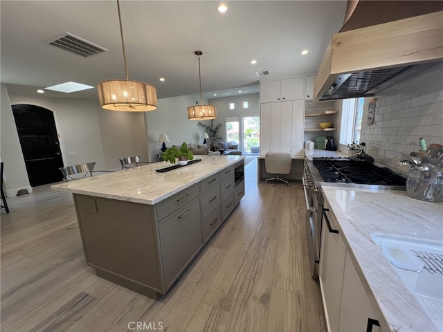 kitchen featuring premium range hood, pendant lighting, a center island, white cabinetry, and stainless steel appliances