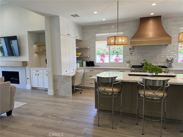 kitchen featuring a breakfast bar area, white cabinetry, backsplash, and wall chimney range hood