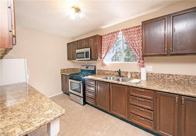 kitchen featuring dark brown cabinets, stainless steel appliances, light stone counters, and sink