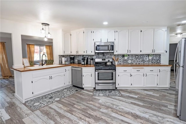 kitchen featuring white cabinets, sink, appliances with stainless steel finishes, decorative light fixtures, and kitchen peninsula