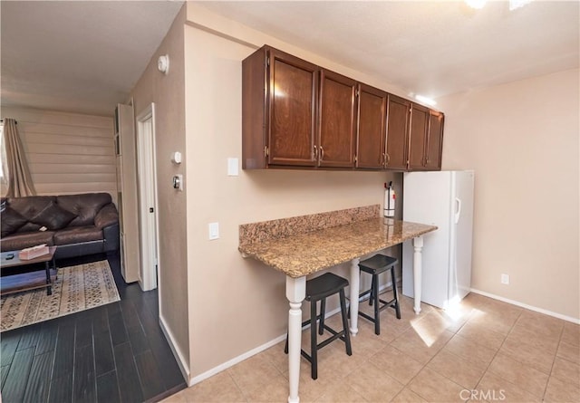 kitchen featuring a breakfast bar, white refrigerator, light stone countertops, and dark brown cabinetry