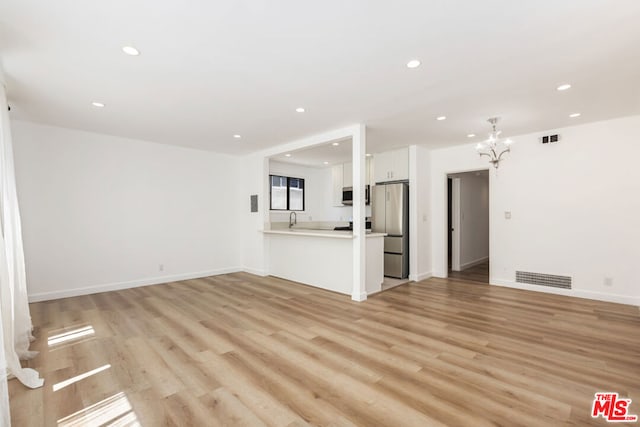 unfurnished living room featuring a notable chandelier, sink, and light hardwood / wood-style flooring