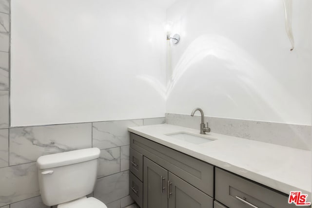 bathroom with vanity, toilet, and tile walls