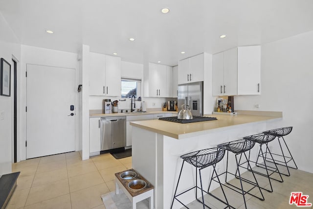 kitchen with appliances with stainless steel finishes, light tile patterned floors, a kitchen bar, and white cabinets