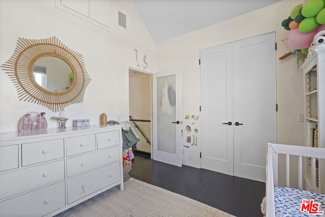 bedroom featuring dark hardwood / wood-style floors, vaulted ceiling, and a crib