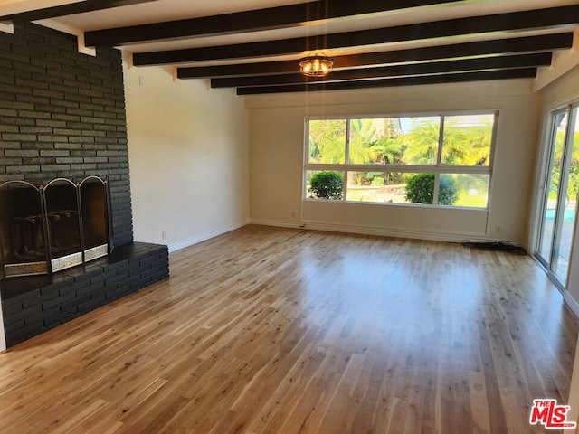 unfurnished living room with a brick fireplace, a wealth of natural light, beamed ceiling, and wood-type flooring