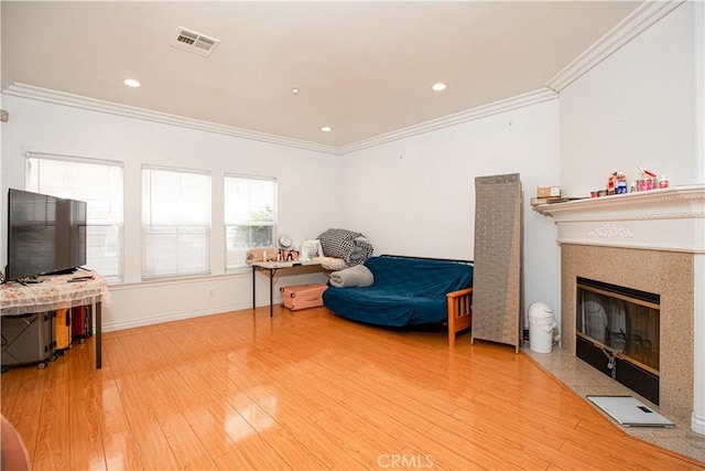 living area featuring hardwood / wood-style floors, ornamental molding, and a tiled fireplace