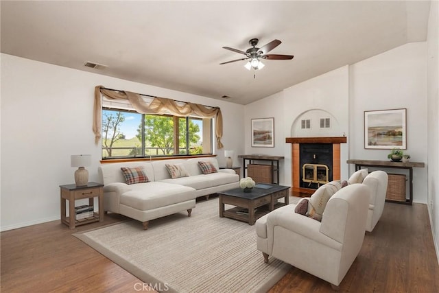 living room with ceiling fan, a tile fireplace, vaulted ceiling, and dark hardwood / wood-style floors