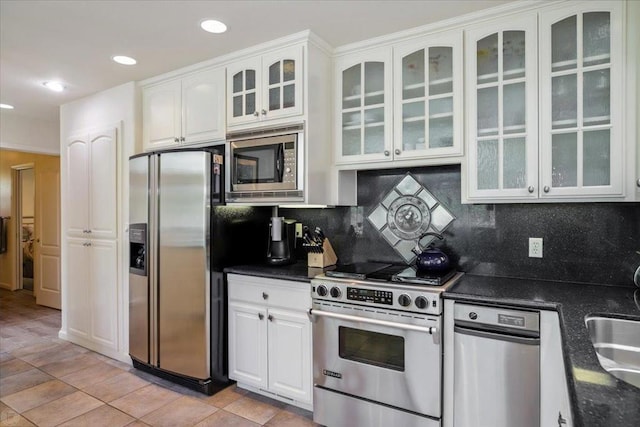 kitchen with light tile patterned floors, stainless steel appliances, tasteful backsplash, dark stone counters, and white cabinets