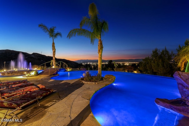 pool at dusk with a patio and pool water feature