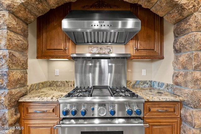 kitchen featuring wall chimney range hood, stove, and light stone countertops