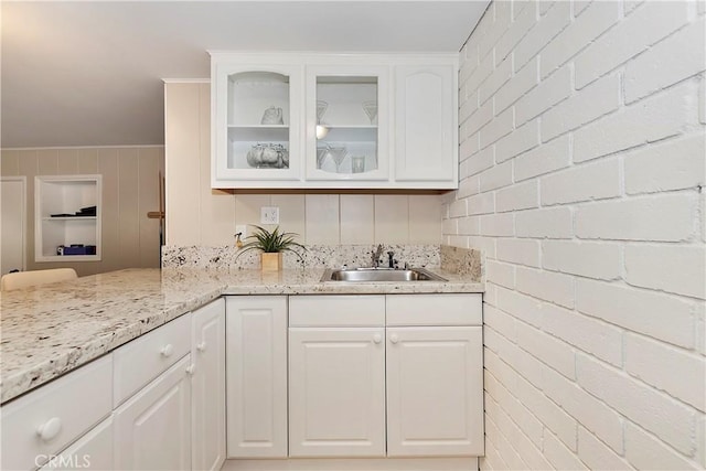 kitchen featuring brick wall, white cabinetry, light stone countertops, and sink