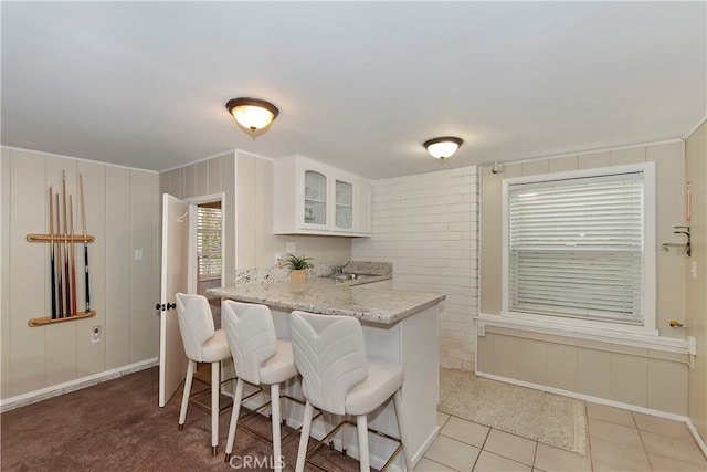 kitchen with kitchen peninsula, tile patterned floors, light stone counters, white cabinets, and a breakfast bar area