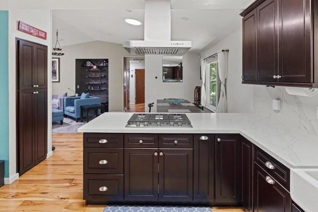 kitchen featuring stainless steel gas cooktop, kitchen peninsula, island range hood, dark brown cabinets, and light wood-type flooring