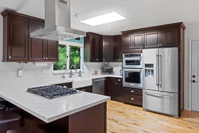 kitchen featuring appliances with stainless steel finishes, light wood-type flooring, a skylight, sink, and exhaust hood