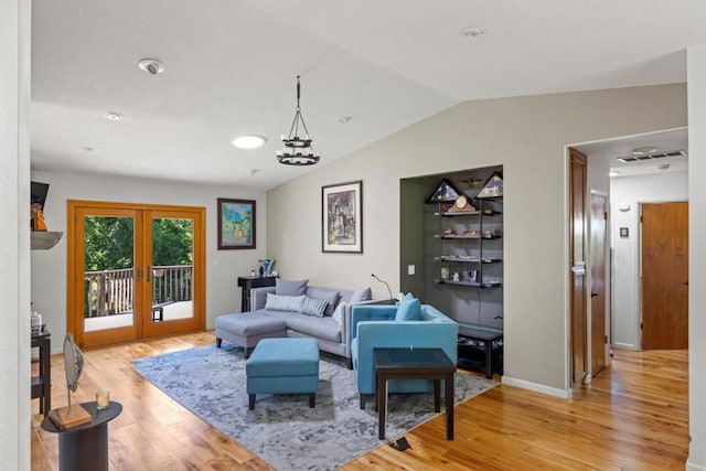 living room with a chandelier, vaulted ceiling, light hardwood / wood-style flooring, and french doors