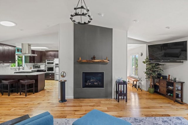 living room with a fireplace, light hardwood / wood-style floors, an inviting chandelier, and lofted ceiling