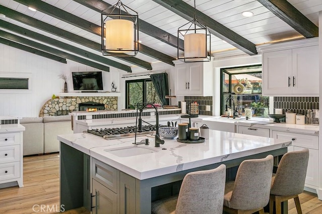 kitchen with a kitchen island with sink, white cabinets, hanging light fixtures, light stone countertops, and a fireplace