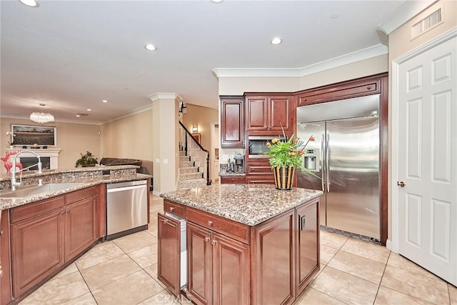 kitchen with sink, light stone counters, built in appliances, crown molding, and light tile patterned flooring