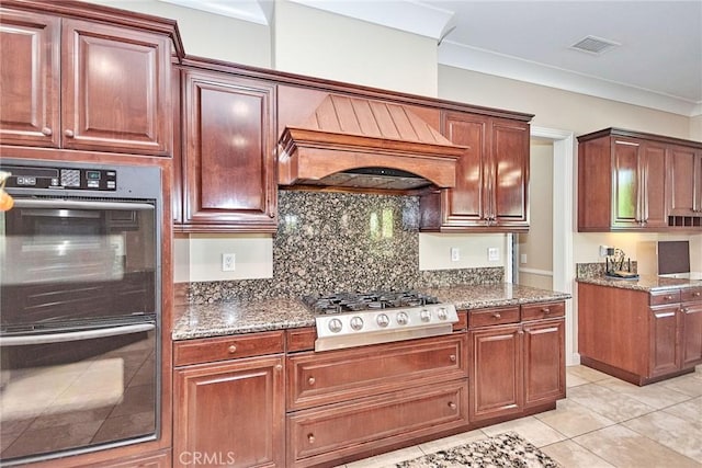 kitchen featuring double oven, dark stone countertops, stainless steel gas stovetop, light tile patterned flooring, and custom range hood