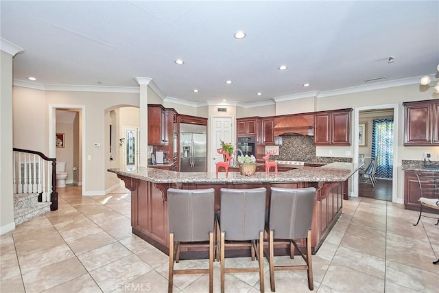 kitchen featuring a kitchen breakfast bar, ornamental molding, stainless steel built in refrigerator, custom range hood, and a center island with sink