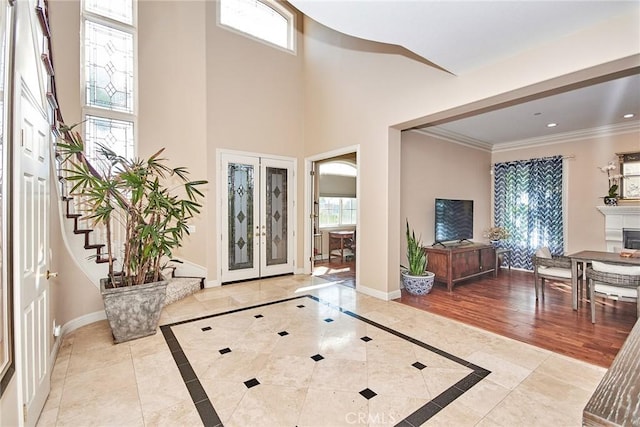 foyer entrance with crown molding, light hardwood / wood-style flooring, a high ceiling, and french doors