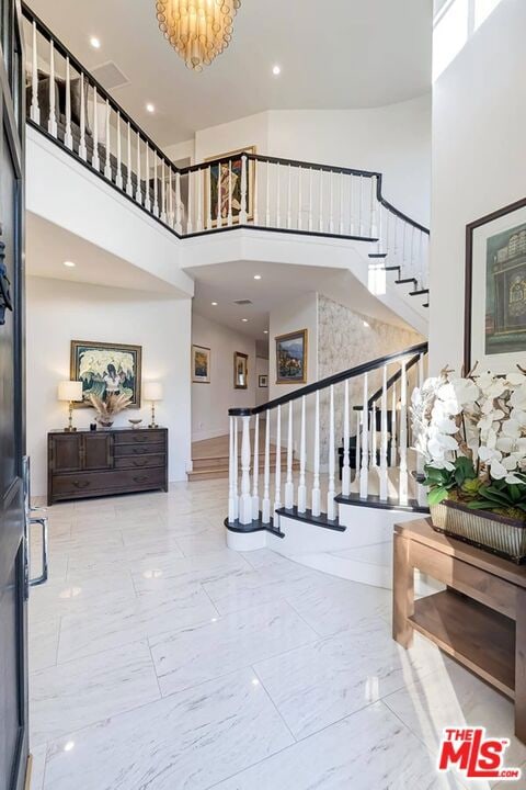 stairway with an inviting chandelier, a towering ceiling, and light tile flooring