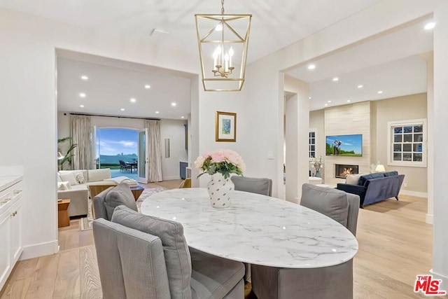 dining space featuring a large fireplace, a chandelier, and light hardwood / wood-style floors