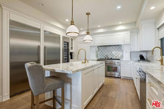 kitchen featuring decorative light fixtures, tasteful backsplash, a kitchen island with sink, hardwood / wood-style floors, and premium appliances