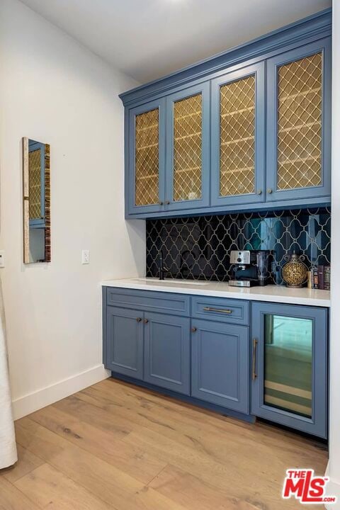 bar with blue cabinets, light wood-type flooring, and tasteful backsplash