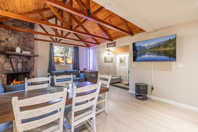 dining room with vaulted ceiling with beams, light hardwood / wood-style floors, a stone fireplace, and wood ceiling